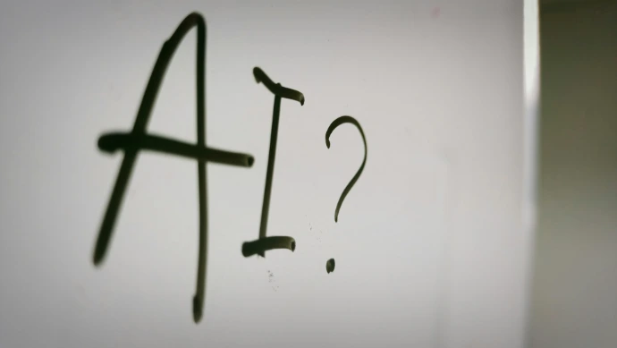 The letters AI and a question mark written in black marker on a whiteboard